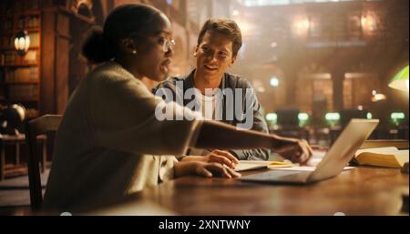 Engaged Multiethnic Students Collaborating on a Project in a Historic Library, Young Man and Woman Using Laptop and Discussing Academic Work Surrounded by Books. Stock Photo