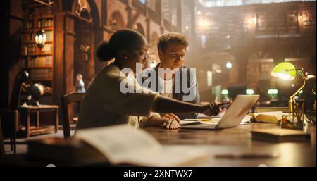 Engaged Multiethnic Students Collaborating on a Project in a Historic Library, Using Laptop and Discussing Academic Materials. Young Man and Woman Focused on Learning Together Amidst Books. Stock Photo