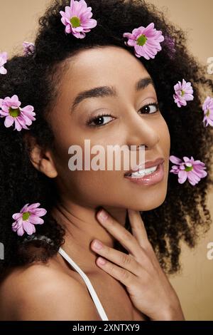 A beautiful African American woman with natural makeup and flowers in her hair smiles softly against a beige background. Stock Photo