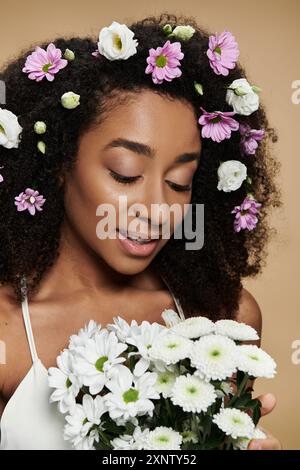 A beautiful African American woman with flowers in her hair, embracing a bouquet of white daisies. Stock Photo