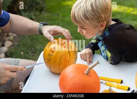 Dad and son carve a Halloween pumpkins on a table in the backyard. The child watches the creative process with interest Stock Photo