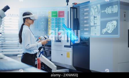 Female Engineer Wearing Virtual Reality Headset and Operating a Heavy Industry Machine with Controllers at a Factory. Digital Visualization of a Technician Configuring Industrial Machinery with VR Stock Photo