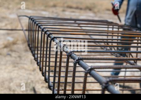 A worker uses steel tying wire to fasten steel rods to reinforcement bars. Close-up. Reinforced concrete structures - knitting of a metal reinforcing Stock Photo