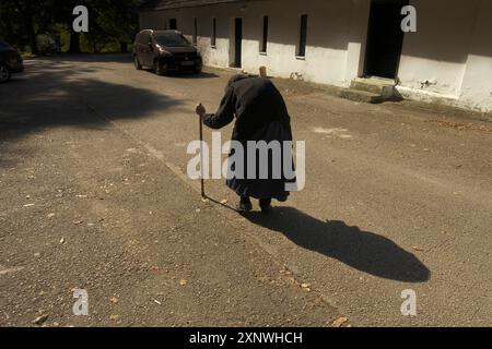 a hundred-year-old woman walks slowly, bent over on her cane, Vracevsnica Monastery, Gornji Milanovac, central Serbia Stock Photo