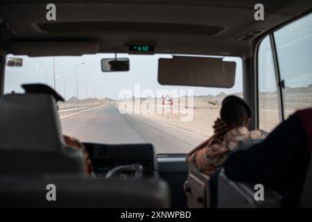 Shot of a bus interior with a view of a desert road and a camel sign ahead in Oman. Represents a journey through isolated landscapes and caution in remote areas. Stock Photo