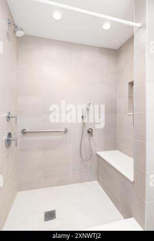 A brown tiled walk-in shower with a chrome faucet, bench seat, and square tiled floor. Stock Photo