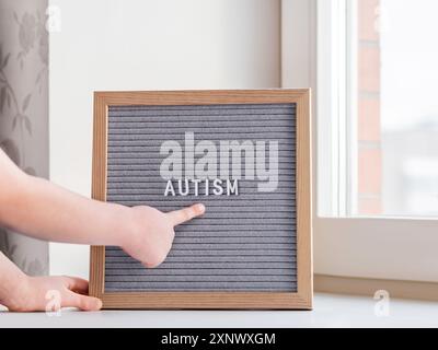 Kid points on grey letterboard with word Autism. Medical diagnosis which usually made in childhood. Drawing attention to development of children. Stock Photo