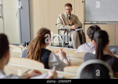 Adult male professor using wheelchair lecturing university students while holding microphone speaking with audience Stock Photo