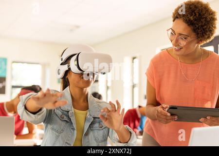 In high school, student using VR headset while teacher with tablet watching Stock Photo