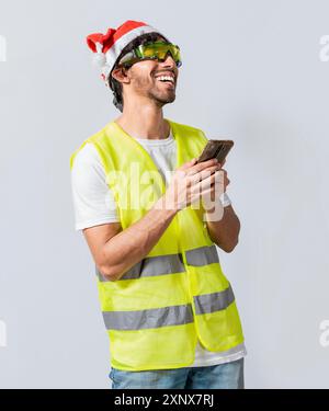 Happy Engineer in christmas hat using cell phone isolated. Smiling engineer in christmas hat using cell phone. Concept of engineer with christmas hat Stock Photo