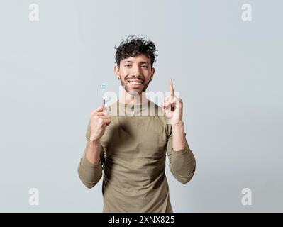 Smiling young man holding dental brush pointing up. Handsome guy holding toothbrush pointing an advertisement up Stock Photo