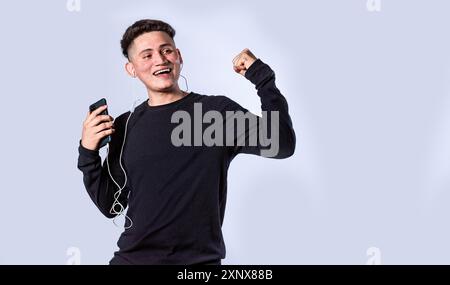 Happy guy with headphones raising hands in victory sign isolated. Young man with cellphone raising hand excited isolated Stock Photo
