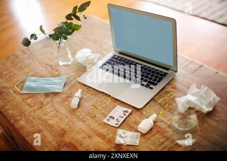 From above various drugs and medical mask placed on table near plant twigs in vase and laptop with blank screen Stock Photo