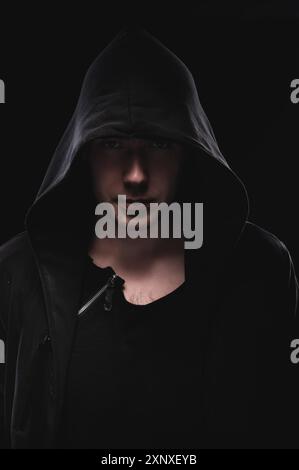 A low key portrait of a man in a hooded hand gesture makes a sperm hero mask. The concept of anonymity and privacy Stock Photo