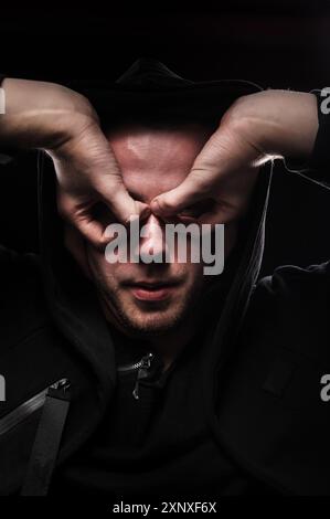 A low key portrait of a man in a hooded hand gesture makes a super hero mask. The concept of anonymity and privacy Stock Photo