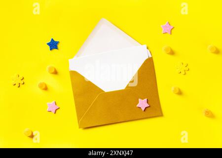 A white greeting card in a golden envelope, shot from the top on a yellow background with stars and glitters Stock Photo