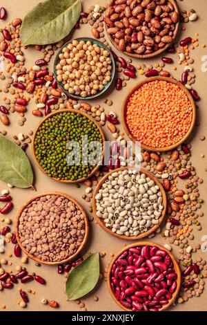 Various legumes, top shot on a brown background. Lentils, soybeans, chickpeas, red kidney beans and other pulses, a flat lay with bay leaves Stock Photo
