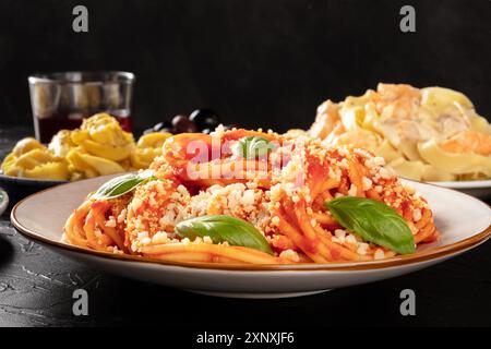 Pasta with tomato sauce, basil and Parmesan, a close-up in a restaurant with other blurred food and wine in the dark background, selective focus Stock Photo