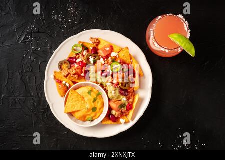 Mexican nachos with chili con carne and a Paloma cocktail, overhead shot on a black background Stock Photo