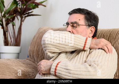 Elderly people sneezing, coughing into her sleeve or elbow to prevent spread Covid-19. Corona virus, sick senior man has flu, sneezing covering nose Stock Photo