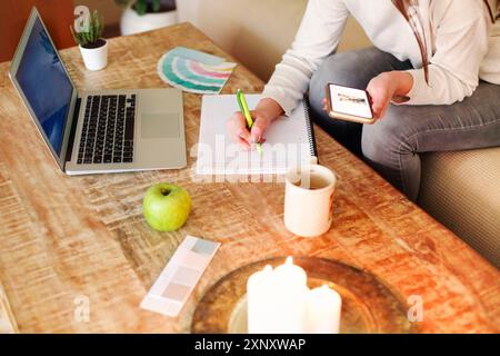 Happy woman in casual clothes sitting on couch and browsing smartphone while working on remote project at home. Close up Stock Photo