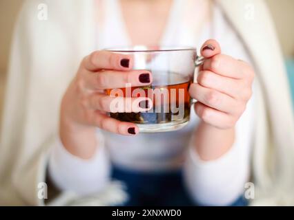High angle of crop female in casual outfit holding glass cup with aromatic herbal tea while relaxing at home Stock Photo