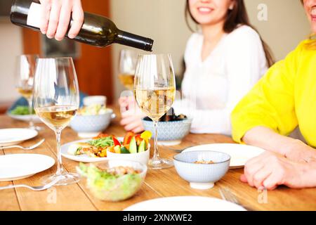 Crop anonymous male standing at table with various dishes and pouring wine into glass during home party with friends Stock Photo