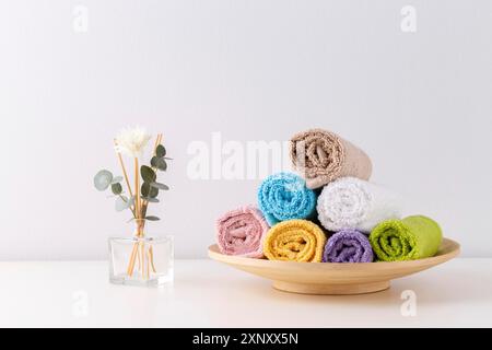 Stack of rolled colorful bath towels on the shelf over light grey background Stock Photo