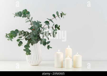 Bouquet of eucalyptus in the ceramic vase and candles on the white table against grey wall, minimalist interior design Stock Photo