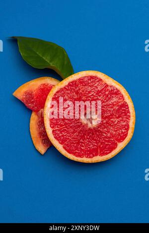 Sliced sides of a grapefruit, three pieces with a green leaf, red pulp isolated on a blue background, vertical shot Stock Photo