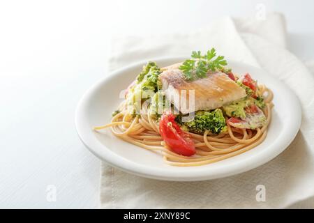 Wild salmon fillet on whole grain spaghetti with broccoli, tomatoes and parsley garnish, healthy seafood meal on a white plate, copy pace, selected Stock Photo