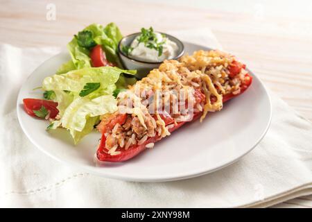 Red bell pepper baked with rice, tuna, tomatoes and cheese, lettuce salad and dip on a white plate and napkin Stock Photo