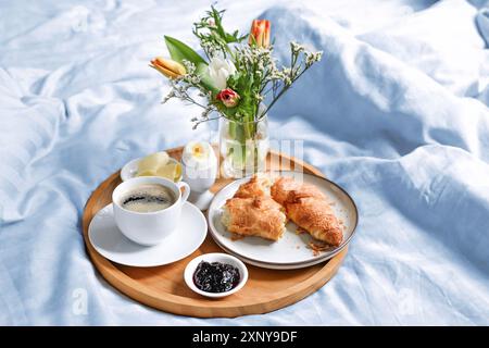 Happy morning with breakfast in bed, flowers, croissant, coffee and more on a tray on blue white linen at birthday, valentines or mothers day, copy Stock Photo