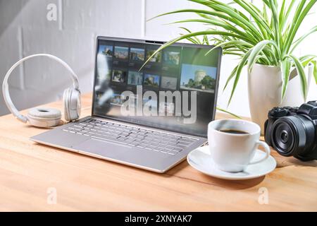 Desk from a media designer with laptop, camera and headphones, also a coffee cup and a plant on the wooden table against a white wall, concept for Stock Photo
