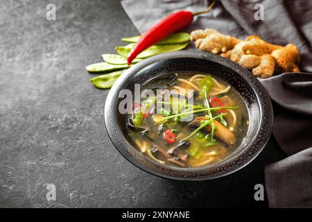 Asian vegetable soup with noodles, mushrooms, sugar peas, nori, ginger and chili, traditionally seasoned with miso paste in a black ceramic bowl on a Stock Photo