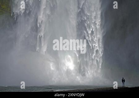 A man stands in front of an impressive waterfall, surrounded by splashing spray, Skogafoss, Iceland Stock Photo