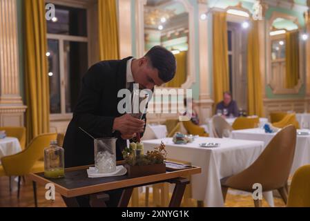Luxurious Hotel Dining Room with Waiter Preparing Drink at Table-Side Cart Stock Photo
