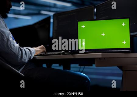 Engineer in server hub using isolated screen laptop to repair equipment storing datasets. Professional using chroma key notebook to do debugging on rigs doing computational operations Stock Photo
