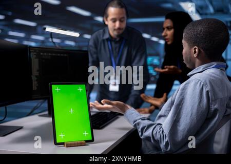 Focus on green screen tablet used by team in blurry background reconfiguring server farm to optimize it for data processing. Close up of mockup device used by workers overseeing data center equipment Stock Photo