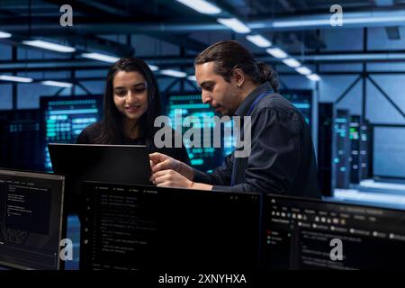 Programmers in data center using laptop to check for server performance issues, talking about solutions. Colleagues in server hub workplace fixing insufficient memory errors slowing down hardware Stock Photo