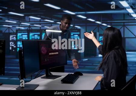 Woman in server farm calling coworker for help, trying to protect gear from hacker stealing information. IT professional in data center requesting assistance to fix security breach alert Stock Photo