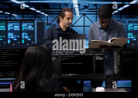 Manager inspecting team of technicians, overseeing data center, looking for firewall misconfigurations. Team leader verifying workers progress in server room, checking if systems bottlenecks are fixed Stock Photo