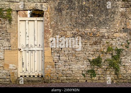 Still life shows a weathered metal door sitting within an ancient, medieval stone wall in France. Stock Photo