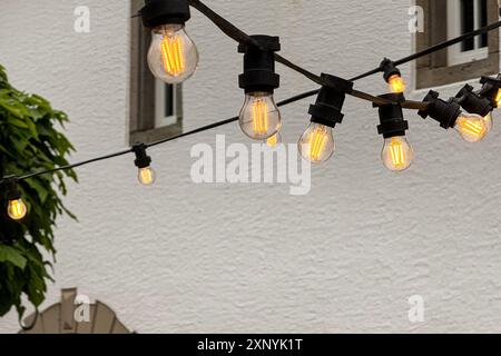 A strand of glowing, decorative Edison light bulbs illuminates a quaint European courtyard at dusk. Stock Photo