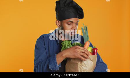 African american cook examining his groceries in a paper bag before preparing a vegan meal, feeling pleased about cooking food with ethically sourced ingredients. Sustainable lifestyle. Camera A. Stock Photo