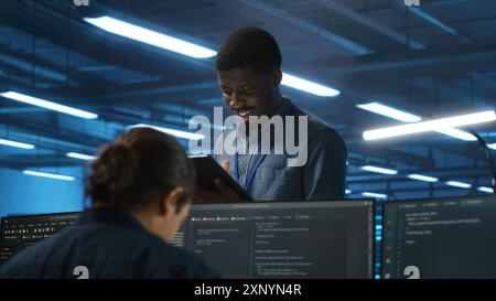 Manager overseeing team and doing system analysis of server farm supercomputers using tablet. Man supervising employees in data center housing storage infrastructure supporting critical IT workloads Stock Photo