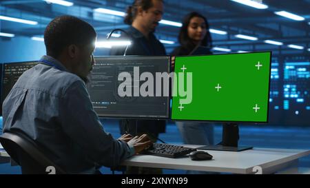IT technician looking at green screen PC, working in data center, ensuring optimal performance. Man monitoring energy consumption across operational server rigs components using chroma key monitor Stock Photo