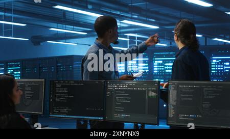 Multiracial team of technicians working in high tech server hub capable of storing vast amounts of data. Coworkers doing brainstorming, trying to troubleshoot servers controlling network resources Stock Photo