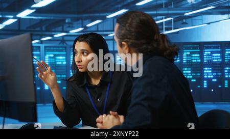 Programmers talking in high tech server hub, using PCs to analyze data. Colleagues examining infrastructure in data center, ensuring system integrity and security, doing brainstorming Stock Photo