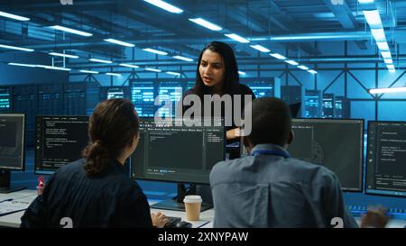 Manager overseeing server room, walking around with checklist on laptop, troubleshooting hardware and discussing with employees. Supervisor doing inspection in server hub, taking feedback from workers Stock Photo
